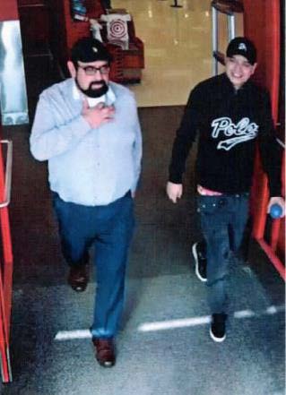 2 men shown exiting target. Man on left has a beard and dressed in black baseball cap, glasses, light blue dress shirt, jeans and dress shoes. Man on right dressed in black baseball cap, black sweater and jeans with black tennis shoes.